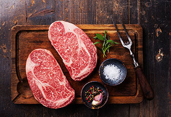 Well marbeled cut of beef steak on a butcher block cutting board with seasonings and utensils